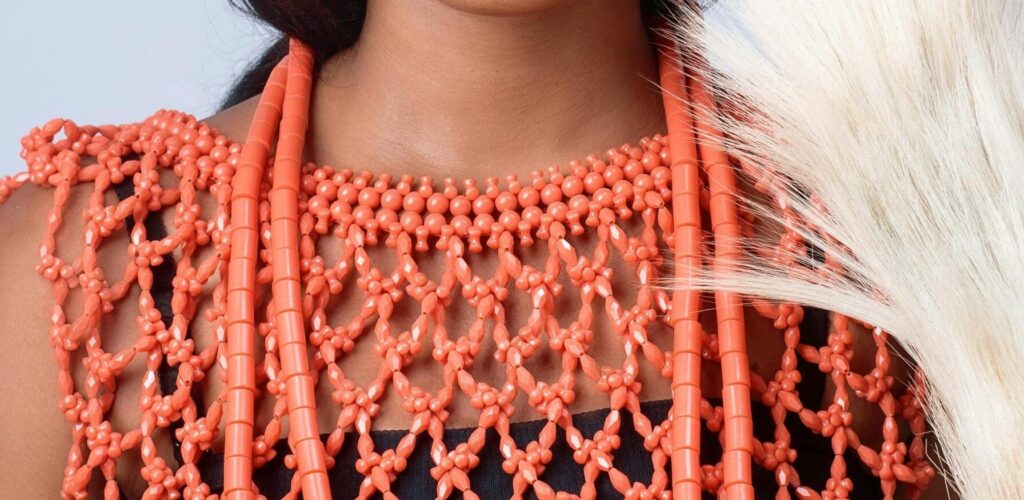 Portrait of a smiling woman in traditional African attire with a coral crown and beads.